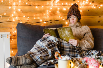 Reading book on cozy sofa in warm house.