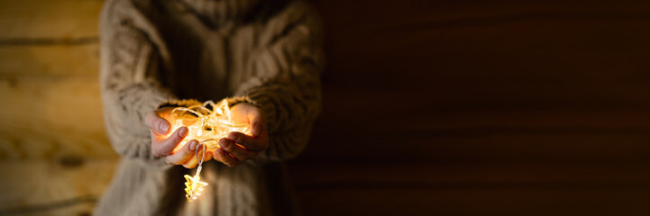 Female hands holding Christmas light decorations on wooden background. Xmas and New Year theme.