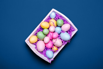 Multicolor eggs in a white tray. Creative Easter concept. Modern solid classic blue background. Horizontal