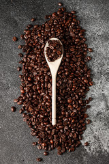 Wooden spoon with coffee on a coffee beans background. Close up. Dark concrete. Top view. Empty space.