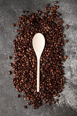 Empty wooden spoon on a coffee beans background. Dark concrete. Top view. Empty space.