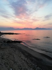 the sun setting behind the promontory with the sea in the foreground