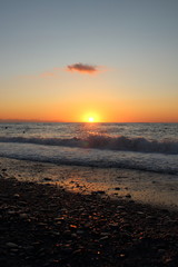Fototapeta premium the sun setting behind the promontory with the sea in the foreground