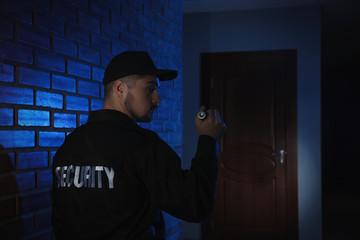 Fototapeta na wymiar Male security guard with flashlight in dark corridor