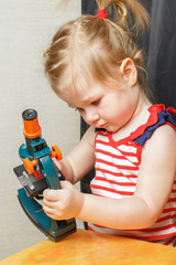A little girl is studying a children's toy microscope.