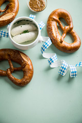 Münchener Weißwurst in Terrine und Brezel mit Oktoberfest Luftschlangen auf Pastell grünen Hintergrund