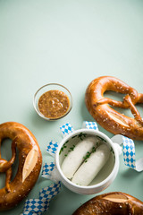 Münchener Weißwurst in Terrine und Brezel mit Oktoberfest Luftschlangen auf Pastell grünen Hintergrund