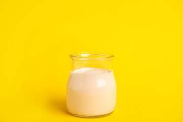 Tasty organic yogurt in glass jar on yellow background