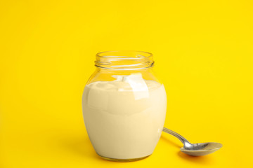 Tasty organic yogurt in glass jar on yellow background