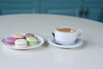 Delicious macaroons and cappuccino on a large bright table in a cozy coffee shop