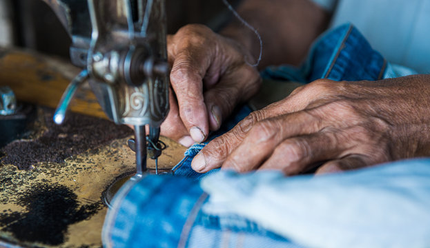 a Taylor at work and his hands of a sewing machine as a close up - Powered by Adobe
