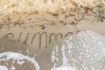 sandy beach with a wave runs onto the word summer