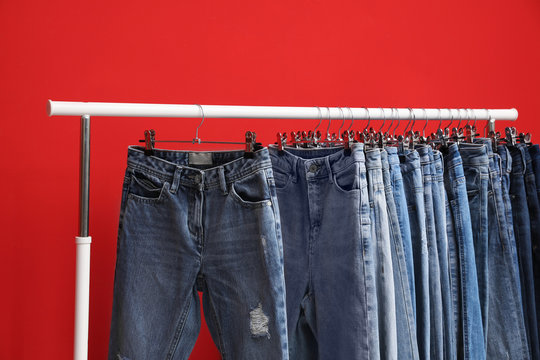 Rack with stylish jeans on red background, closeup