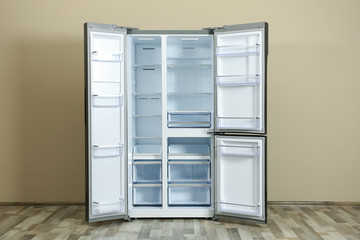 Modern empty refrigerator near beige wall. Home appliance