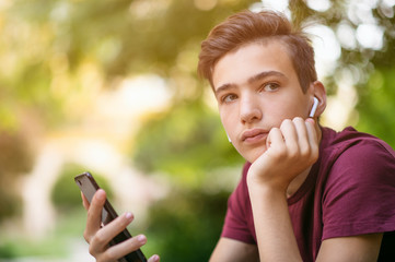 Close-up portrait of a thoughtful unhappy teenage boy with smartphone, outdoors.  Sad teenager with...