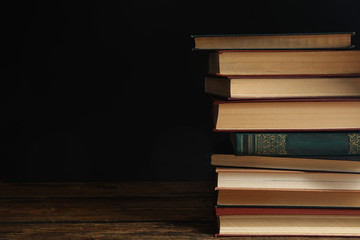 Collection of different books on wooden table against dark background. Space for text