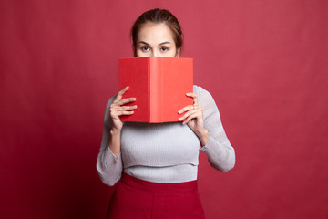 Young Asian woman with a book cover her face.