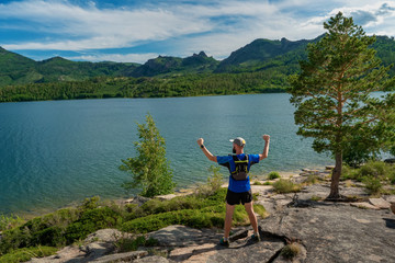 Athlete runner standing on the edge of a cliff overlooking a beautiful mountain lake. Bayanaul National Park. Kazakhstan