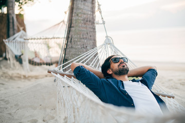 A man enjoys calm, lies in a hammock on the background of the ocean and sunset.