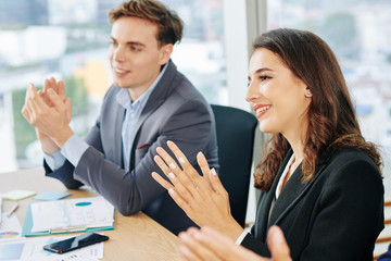 Pretty young business lady attending meeting with coworkers and applauding speaker