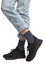 Cropped shot of a man's cross-legs in blue jeans and black sneakers, staying on a white background. It is dark grey socks on his foots. 