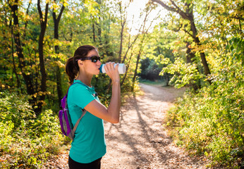 Active young woman drinking water from the bottle in the nature
