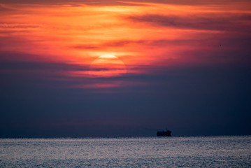 Naklejka na ściany i meble Sunset scene at the sea. Dramatic red sky above the silhouette of a ship in calm sea waters.