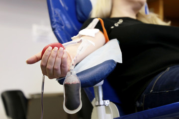 Woman blood donor in chair during donation with a blood bag and red bouncy ball in hand. Concept of donorship, transfusion, health care