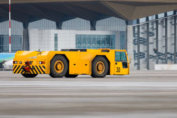 Airplane yellow pushback truck in moving at airport. Special, low profile vehicle - pushback tractors/tugs. Aircraft support maintenance vehicle at airport airside apron with terminal.