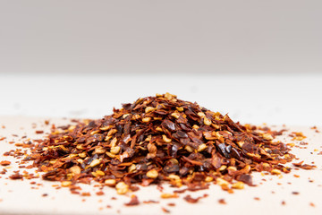 Red pepper flakes on paper background. Exotic paprika chili spice on plate. Dried and crushed red chili peppers. Selective focus.