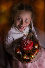 Beautiful girl holds Easter cake and eggs on a plate and smiling at the camera. Easter holiday.