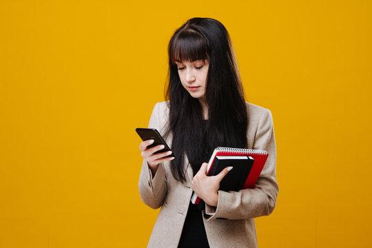 Young Tired Business Woman In A Grey Suit Checking Her Phone Over Yellow