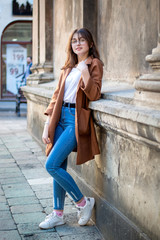 Stylish girl on a walk in the street. Beige raincoat, bag over his shoulder. Image of a modern woman
