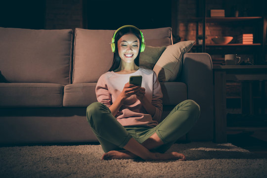 Portrait of her she nice attractive cheerful brunet girl sitting on floor carpet in lotus pose resting listening modern different sound rhythm at night late evening home dark living-room house indoors