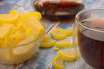 Marmalade lemon slices, a glass of black tea and a teapot with brewed tea on a wooden background. Sweet dessert. Close up.