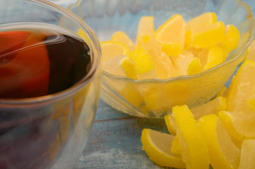 Fototapeta na wymiar Marmalade lemon slices and a glass of black tea on a wooden background. Sweet dessert. Close up.