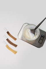 Bowl of die developer on scales next to locks of dyed hair samples. on white