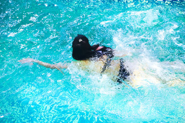 Young girl on black bikini is swimming in the blue pool at the fitness centre. Woman is relaxing after a hard day. Healthy living lifestyle concept.