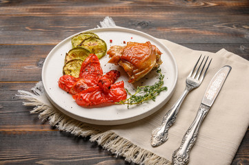 Homemade baked chicken thigh, zucchini and peppers with soy sauce, spices and herbs on a white plate on a wooden background. Close up