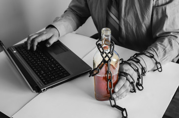 Man's hands in old rusty chains near the bottle. Addicted to alcohol. In the trap of office work. Routine job. Manager near the laptop.