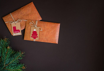 Christmas border on dark background, composed of fresh fir branches and envelope of kraft paper. Merry Christmas and Happy Holidays! Flat lay, top view, copy space.