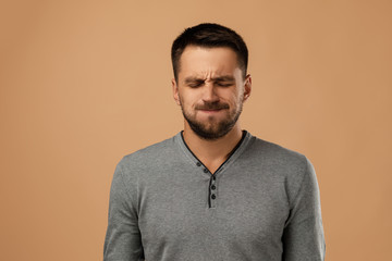 young bearded man with frowns face in casual gray sweater on beige background.