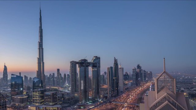 Dubai downtown skyline with tallest skyscrapers and busiest traffic on highway intersection night to day transition timelapse. Aerial view from above