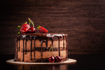 Čokoladna torta s bobičastim voćem, jagodama i trešnjama. kolač na tamno smeđoj podlozi. kopija prostora