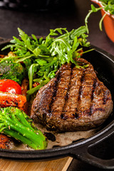 American food concept. Grilled beef steak with grilled vegetables, with carrots, cherry tomatoes, broccoli, in a cast iron pan. copy space