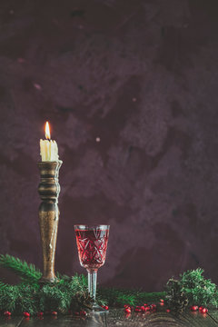 Greeting food Christmas and New Year composition. Vintage glass of pomegranate drink surrounded  pine branches and festive candles, dark background