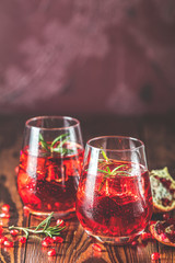 Two glasses of Pomegranate Cocktail Decorated with Rosemary and Ice, Cold Drink on claret bordeaux concrete background.