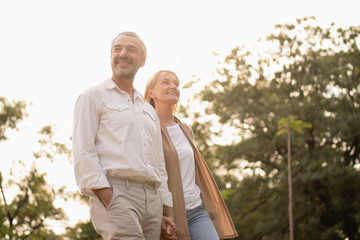 Senior active caucasian couple holding hands looks happy and carefree in the park in the afternoon autumn sunlight with copy space, happily retired spouse, elderly healthy lifestyle,happy anniversary.