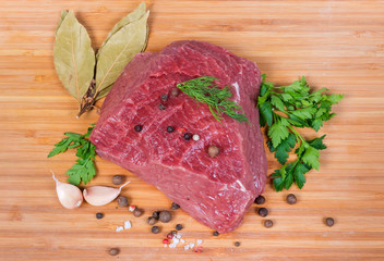Top view piece of uncooked beef among greens and spices