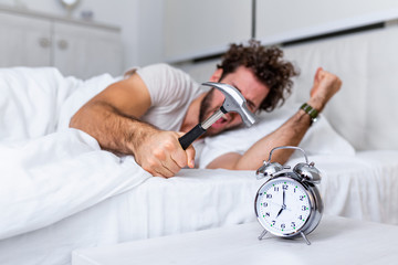 Young man tries to break the alarm clock with hammer, Destroy the Clock. Man lying in bed turning...